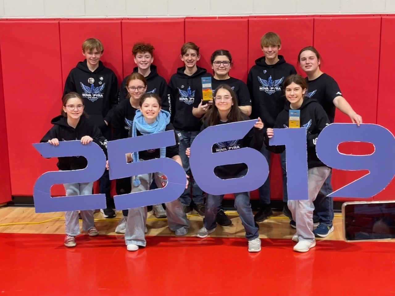 FTC 25619 Nova Pyra team members surrounding their robot 'Bullfrog' with their trophies after their successes at the 2024-2025 FTC LA Qualifier 1 at Hammond Crossroads